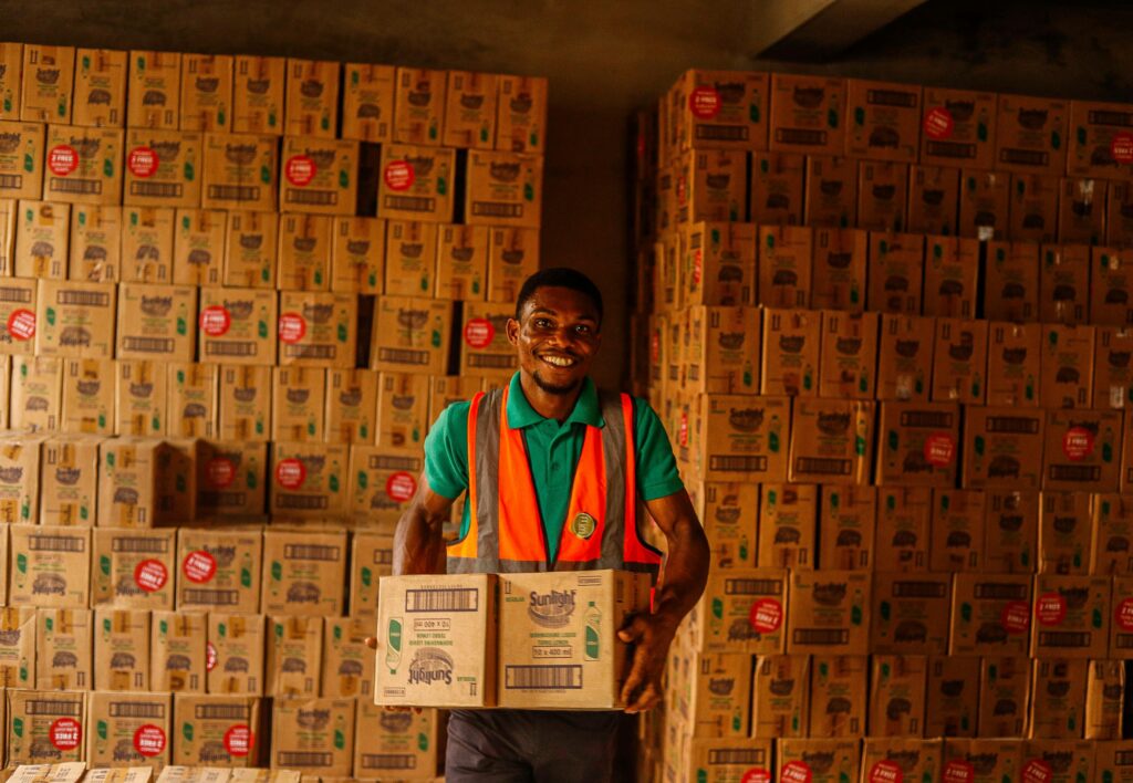 Energetic warehouse worker smiling while holding boxes, representing teamwork and productivity.